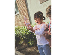 Load image into Gallery viewer, Child holding a pink bottle outdoors with a building in the background