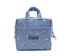 Load image into Gallery viewer, A personalized light blue lunch bag with a space-themed print of rockets, rockets carrying children, hot air balloons, and stars. The name 'Dani' is printed in navy blue on the front pocket.