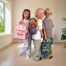Load image into Gallery viewer, Three children standing indoors holding colorful custom school backpacks and a water bottle. The child on the left holds a pink backpack with 'Betty' written on it, the middle child holds a multicolor backpack, and the child on the right holds a blue tropical-print backpack with 'Jack' written on it.