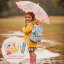 Load image into Gallery viewer, A young girl stands in the rain holding a pink umbrella and wearing a yellow raincoat, blue patterned backpack, and pink rain boots. A circular inset shows a school supply coloring set with pencils and a coloring book.
