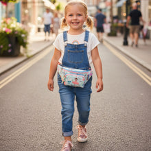 Load image into Gallery viewer, Young girl in denim overalls with a colorful bag walking on a street.